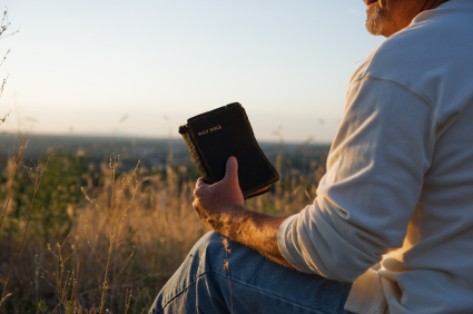 Mies istuu maassa Raamattu kädessään.