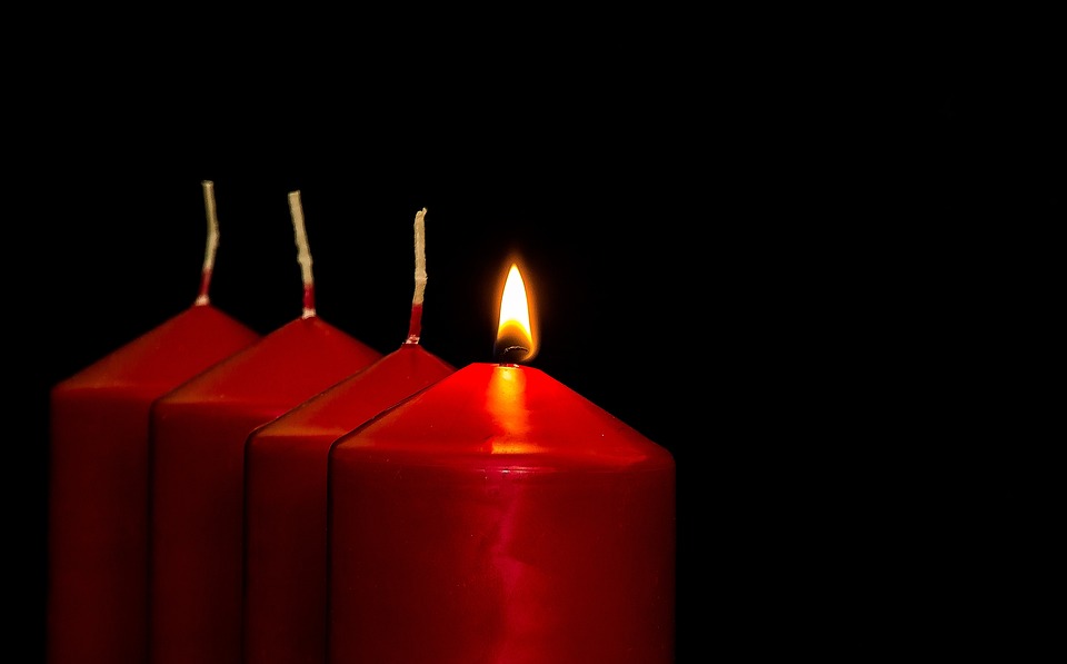 Neljä punaista kynttilää rinnakkain, joista yksi palaa.