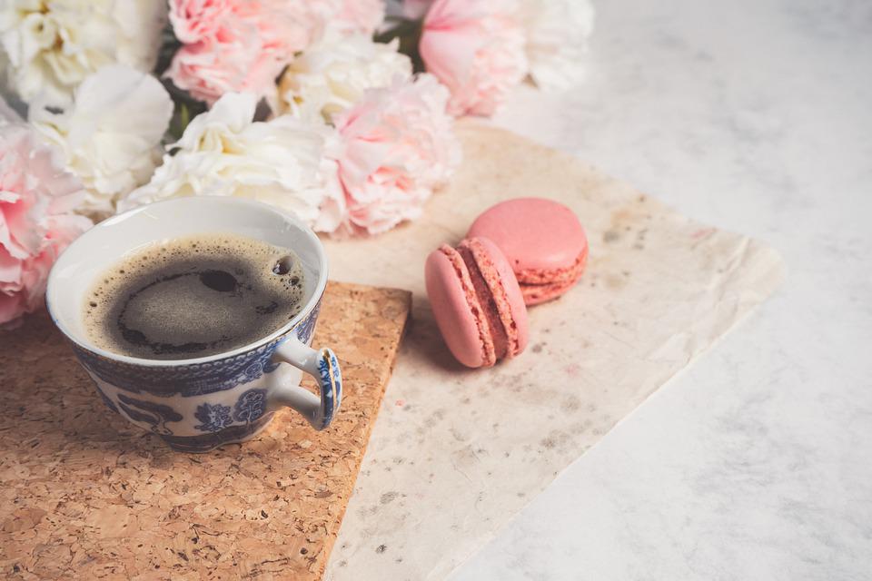 Kuvassa pöydällä kahvikuppi, muutam macarons-leivos ja kukkia.