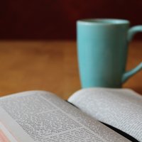 Kuvassa on kahvikuppi ja Raamattu auki.